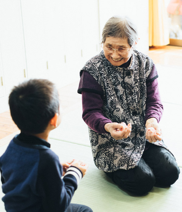 高齢者と子どもが畳の上で交流する様子。世代間交流の活動場面です。
